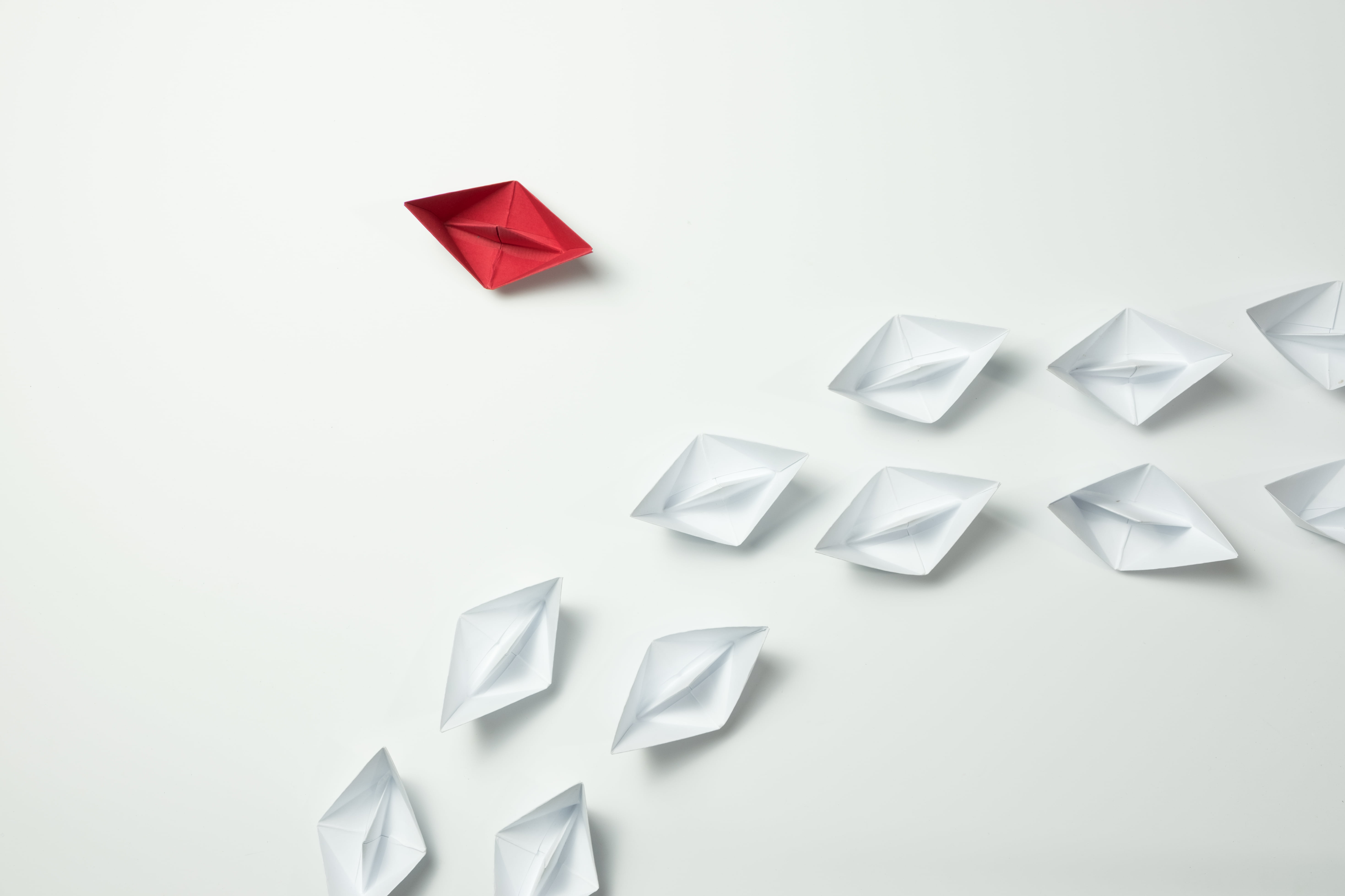 Red paper ship changing direction and white ones. New idea, change, trend, courage, creative solution, innovation and unique way concept.